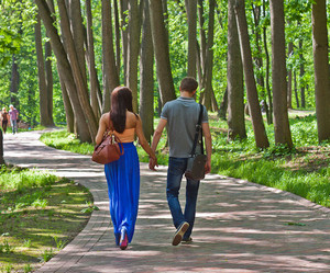 Парень и девушка гуляют за ручку по парку