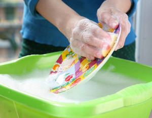 Женщина моет цветную тарелку в зеленом тазике