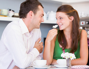 Женщина нюхает белый цветок и смотрит на мужчину